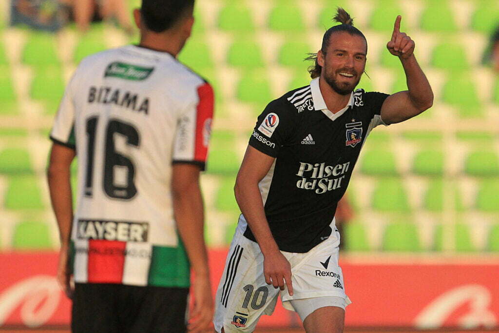 Christian Santos con la camiseta negra de Colo-Colo celebrando con una mano en alto su gol contra Palestino en el Estadio La Cisterna