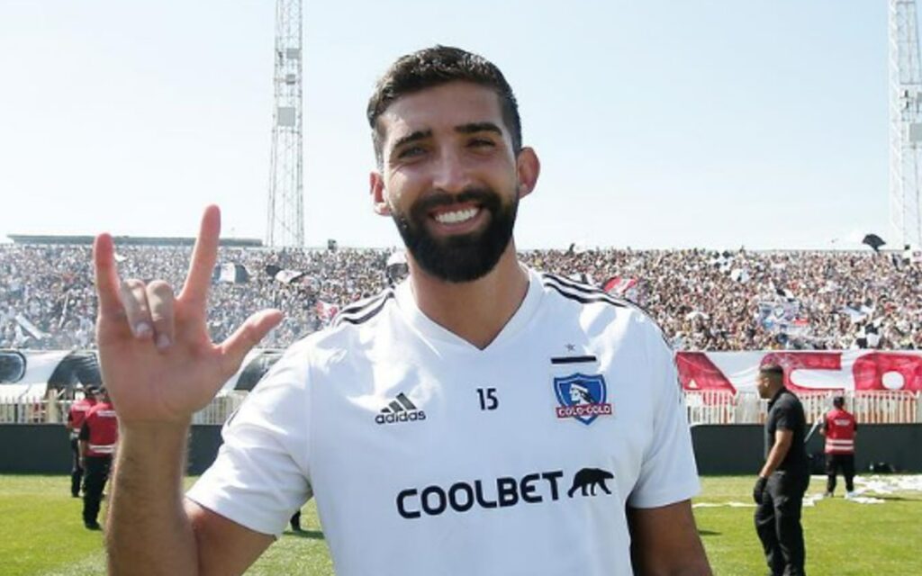 Emiliano Amor con la mano derecha levantada en la cancha del Monumental