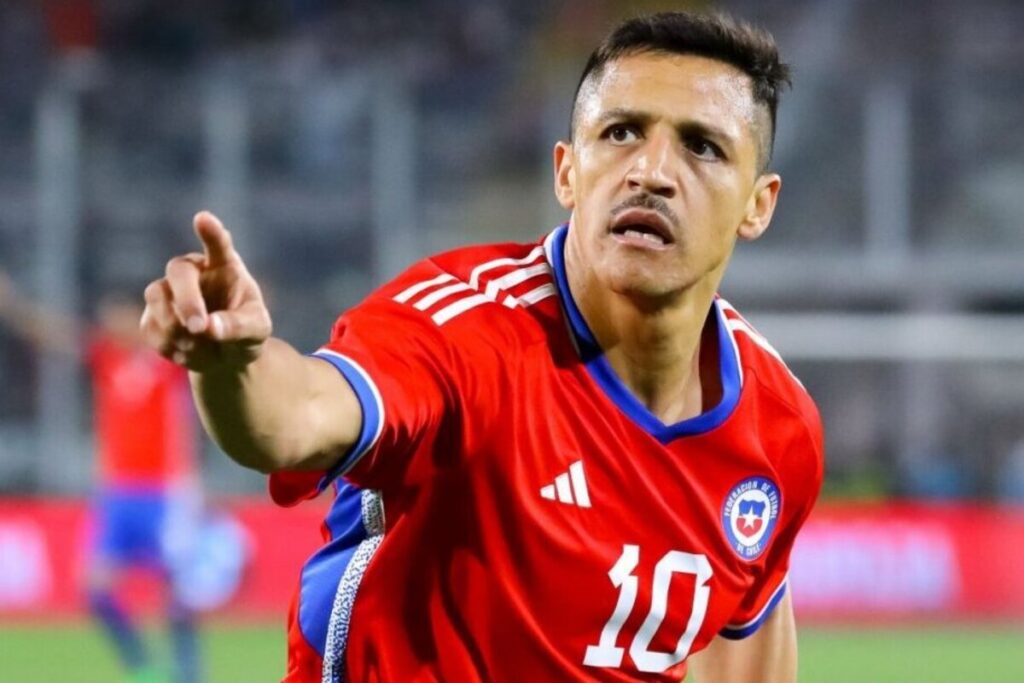 Alexis Sánchez con la camiseta de la selección chilena con su dedo levantado.