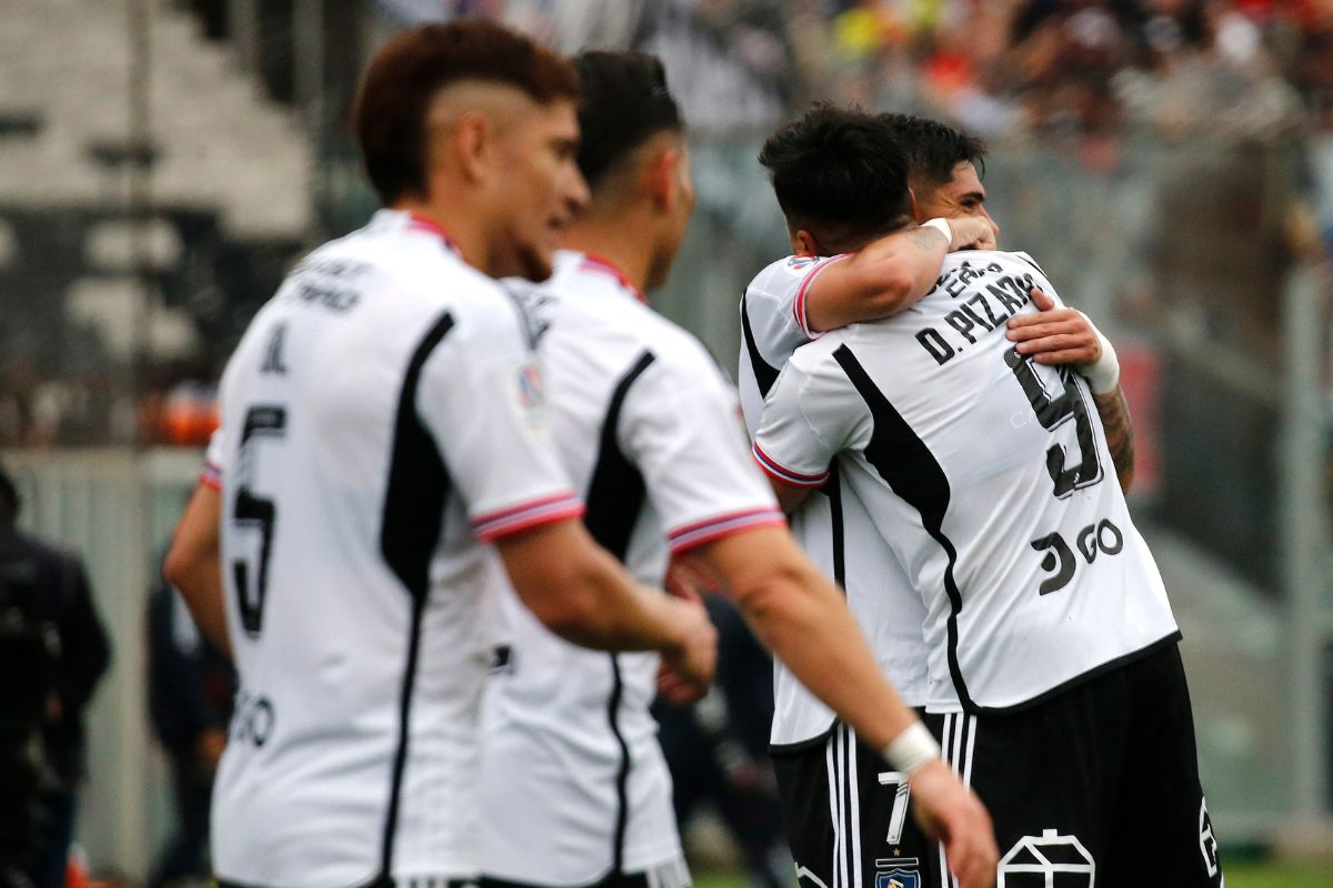 Futbolistas de abrazados mientras usan la camiseta blanca de Colo-Colo