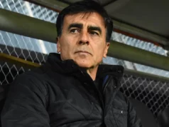 Gustavo Quinteros con la mirada fija y vestido de negro total en una banca de fútbol.
