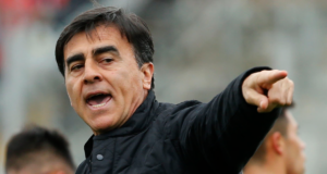 Gustavo Quinteros con la boca semiabierta apunta a algo o alguien con su dedo en medio de un partido de Colo-Colo.