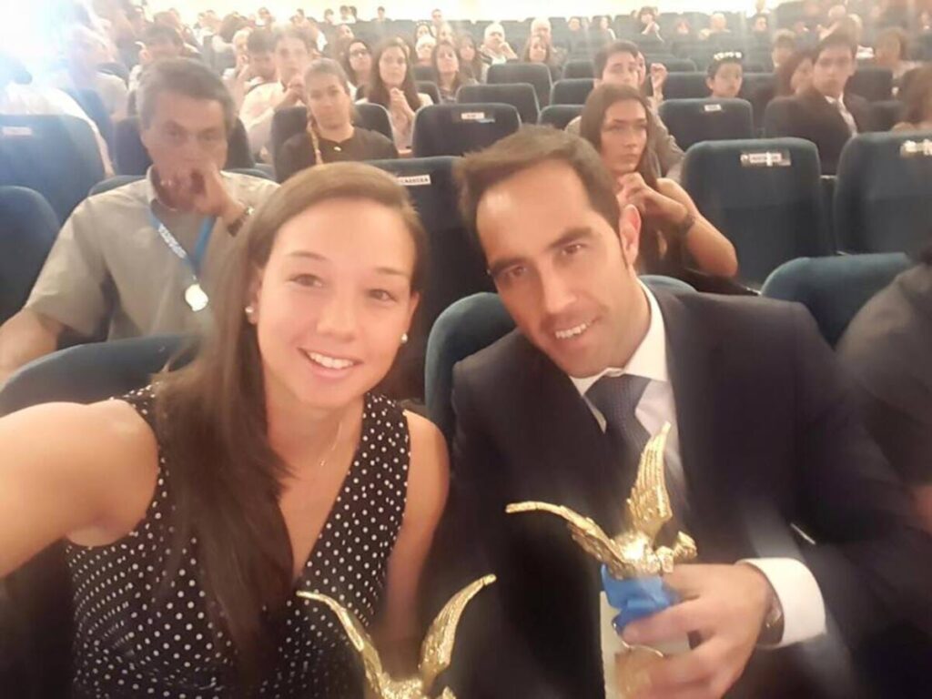 Primer plano a los rostros de Christiane Endler y Claudio Bravo recibiendo un premio en una gala.