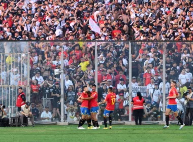 Futbolistas de Unión Española celebran un gol en la cancha principal del Estadio Monumental, mientras que en el fondo aparecen los hinchas de Colo-Colo en el sector Arica.