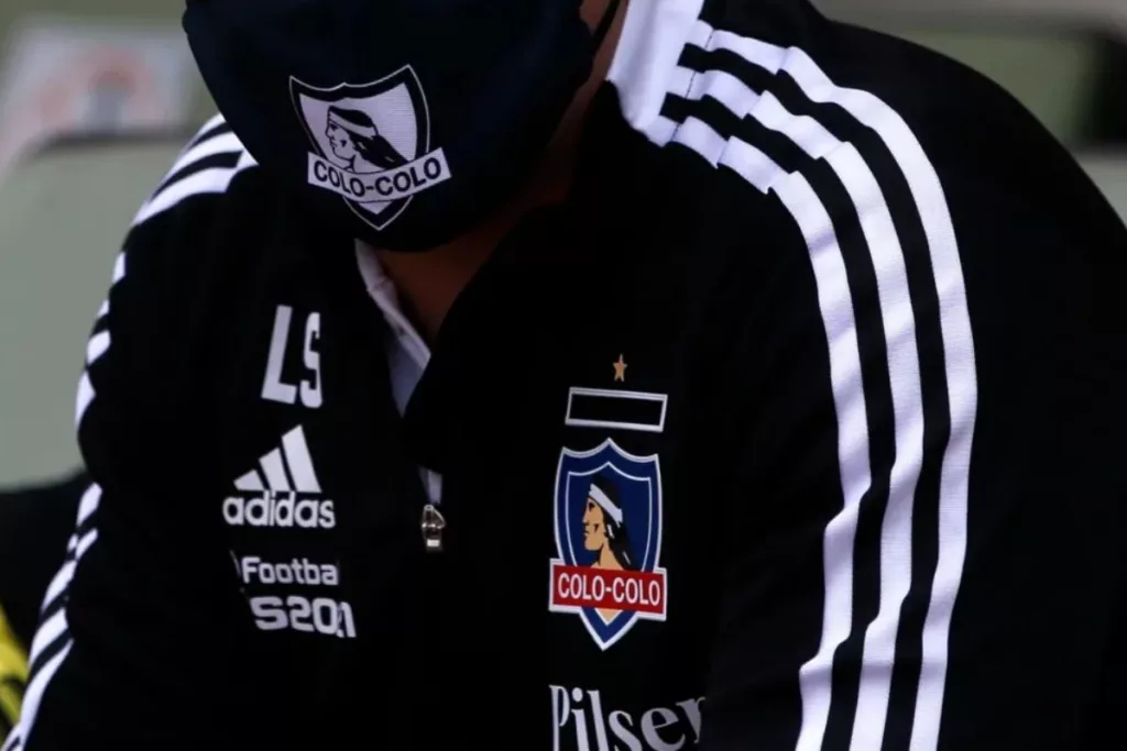 DT con el buzo negro de Colo-Colo y mascarilla con la insignia del club