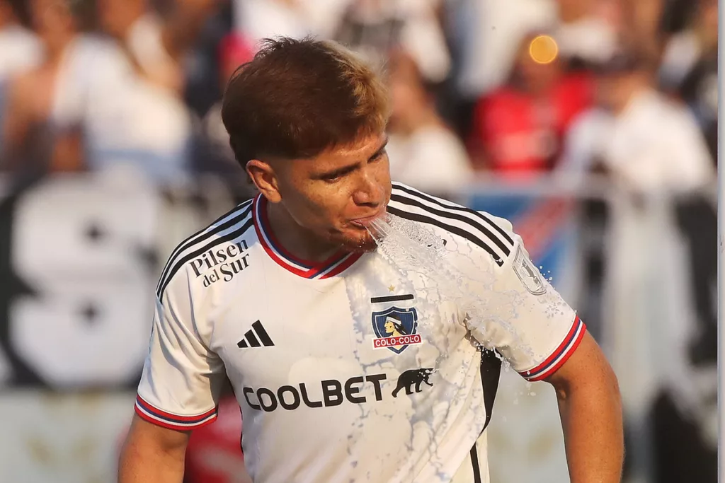 Leonardo Gil escupiendo un chorro de agua en pleno partido con la camiseta de Colo-Colo durante la temporada 2023.