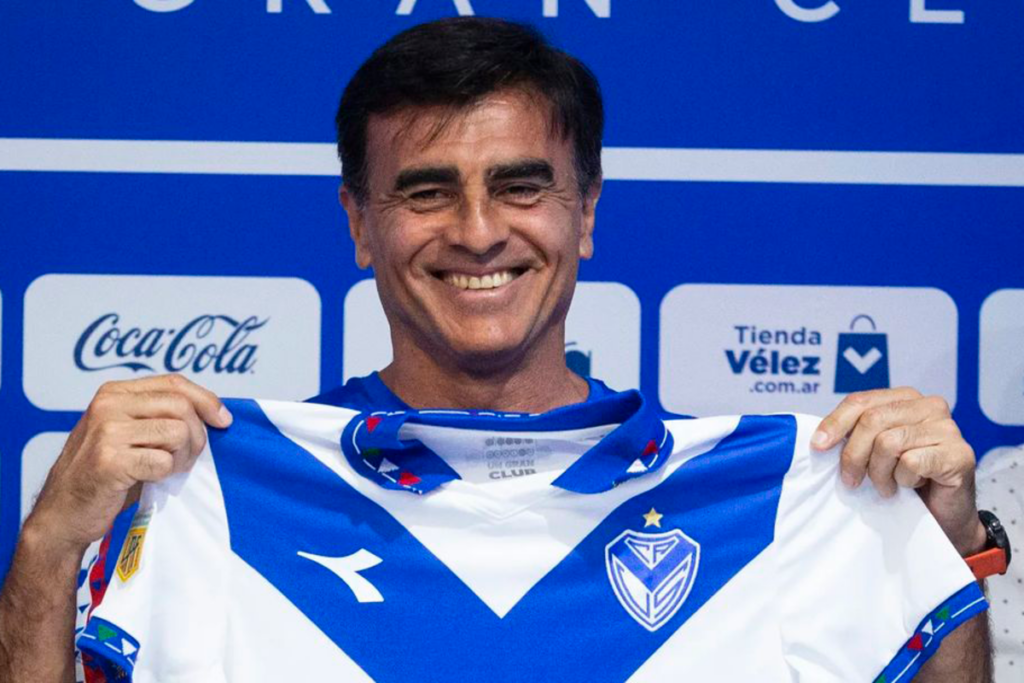Gustavo Quinteros sostiene la camiseta de Vélez Sarsfield y sonríe ante las cámaras en su presentación oficial en el conjunto de Liniers de cara a la temporada 2024.