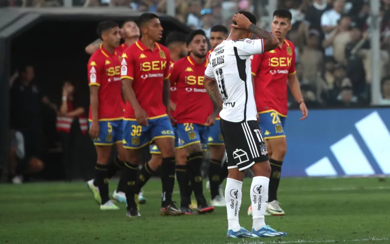 Marcos Bolados tomándose la cabeza mientras jugadores de Unión Española celebran un gol.