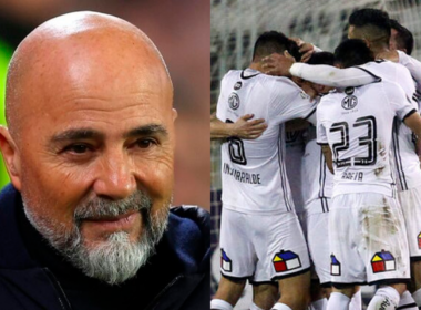 Primer plano al rostro sonriente del entrenador de fútbol profesional, Jorge Sampaoli, mientras que a mano derecha aparecen los jugadores de Colo-Colo celebrando un gol durante la temporada 2018.