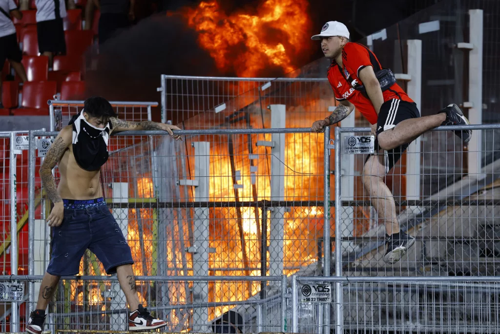 Hinchas de Colo-Colo sobre una reja mientras se quema la galería norte del Estadio Nacional.
