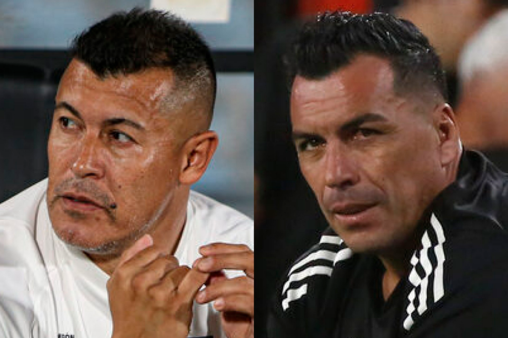 Primer plano a los rostros pensativos de Jorge Almirón y Esteban Paredes, entrenador de Colo-Colo durante la temporada 2024 y ex futbolista profesional, respectivamente.