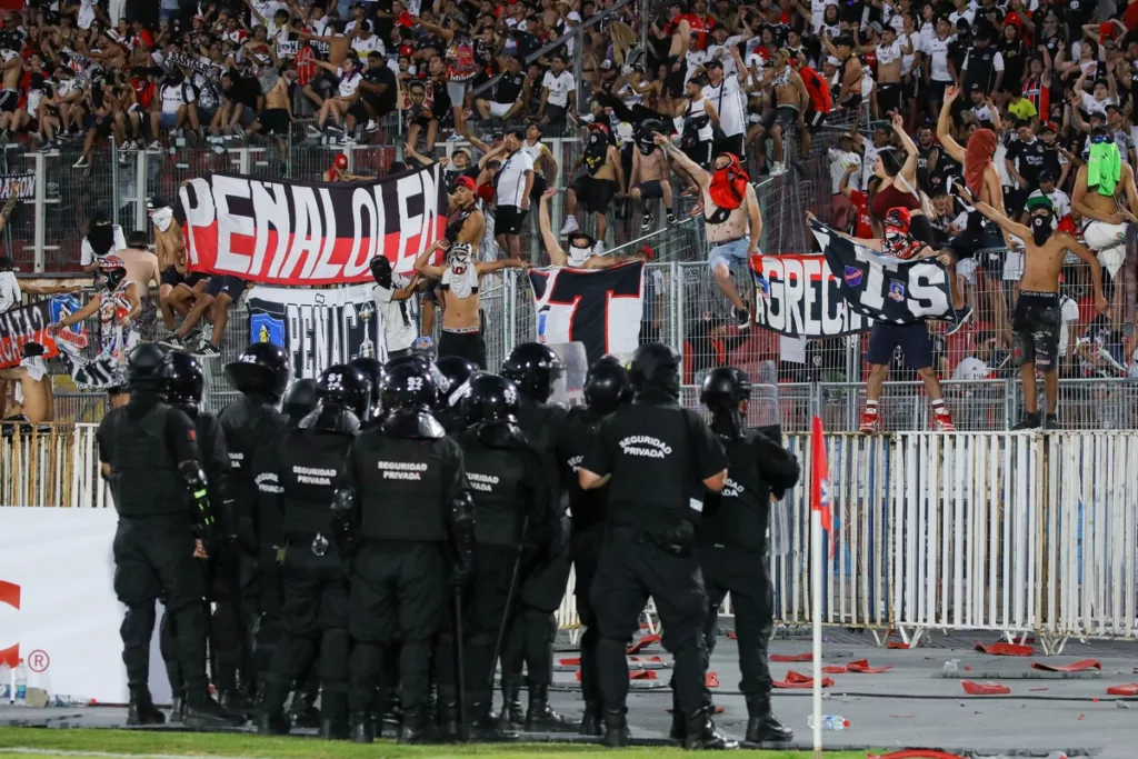 Policía uniformada de Chile mira a los hinchas de Colo-Colo apostados en el sector norte del Estadio Nacional en plenos incidentes en la Supercopa 2024.