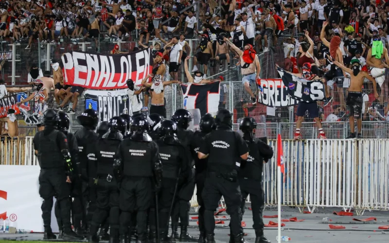 Policía uniformada de Chile mira a los hinchas de Colo-Colo apostados en el sector norte del Estadio Nacional en plenos incidentes en la Supercopa 2024.