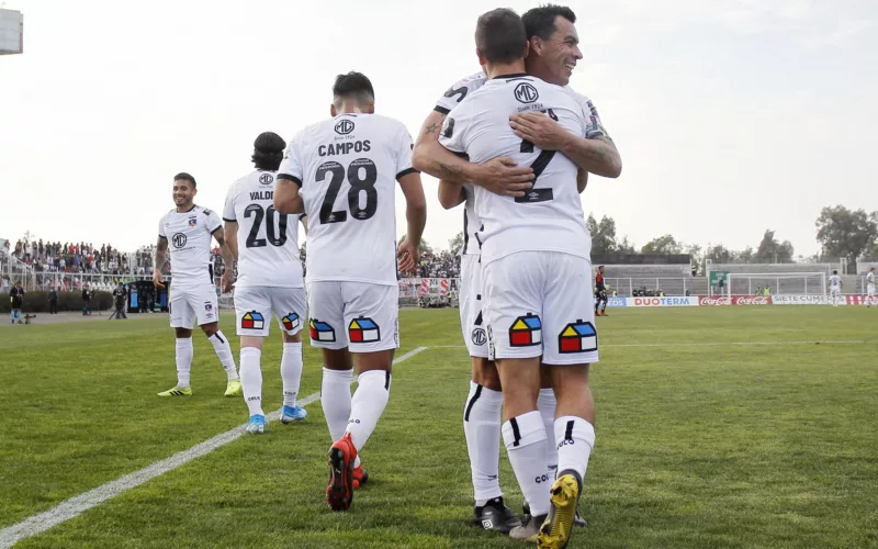 Esteban Paredes abraza a Gabriel Costa tras anotar un gol con la camiseta de Colo-Colo durante la temporada 2019 en el Estadio Municipal de La Cisterna, mientras que el resto de sus compañeros camina al círculo central.