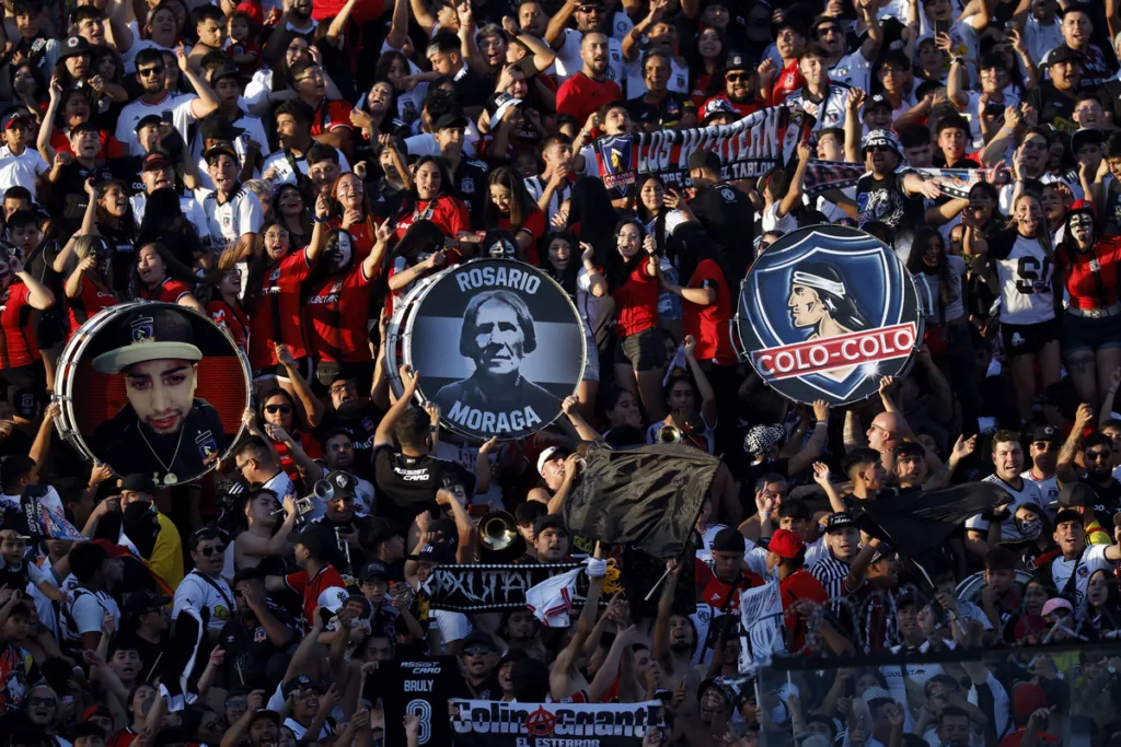 Hinchas de Colo-Colo alientan al equipo y levan tres bombos que representan a la institución durante la temporada 2024.