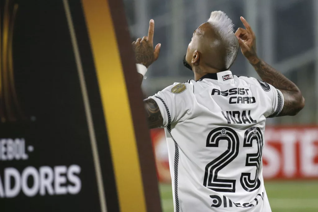 Arturo Vidal de espalda y con los dedos apuntando hacia el cielo con la camiseta de Colo-Colo. A mano izquierda se puede ver un pedazo de cartel de la Copa Libertadores 2024.