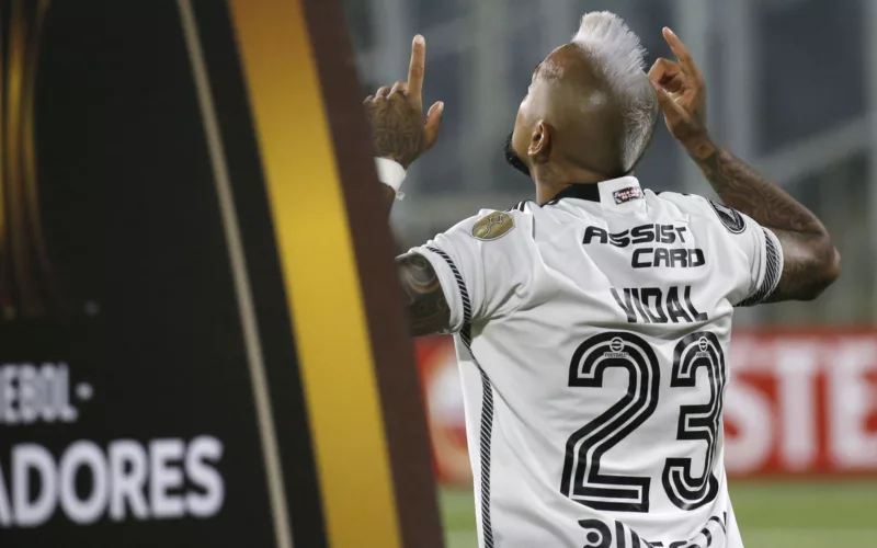 Arturo Vidal de espalda y con los dedos apuntando hacia el cielo con la camiseta de Colo-Colo. A mano izquierda se puede ver un pedazo de cartel de la Copa Libertadores 2024.