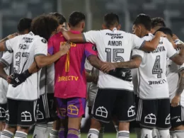 Fotografía a las espaldas de los futbolistas de Colo-Colo masculino durante la temporada 2024, quienes se encuentran abrazados y arengándose antes de jugar un partido.