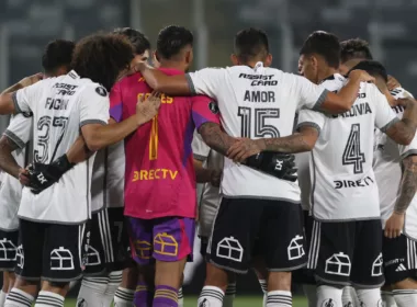 Fotografía a las espaldas de los futbolistas de Colo-Colo masculino durante la temporada 2024, quienes se encuentran abrazados y arengándose antes de jugar un partido.