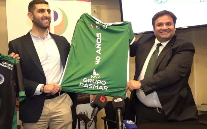 Aziz Mosa junto al presidente de Deportes Puerto Montt levantan una polera del club donde se ve la parte trasera.