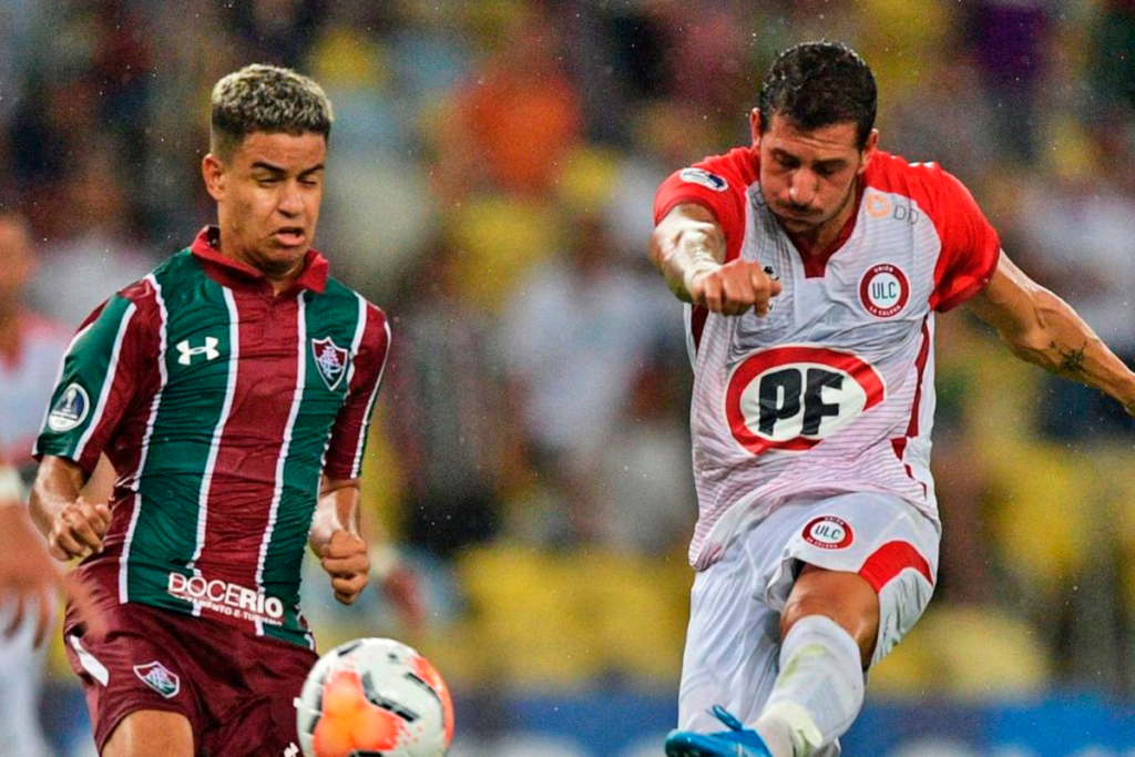 Gonzalo Castellani impactando un balón con la camiseta de Unión la Calera ante la atenta mirada de un jugador de Fluminense.