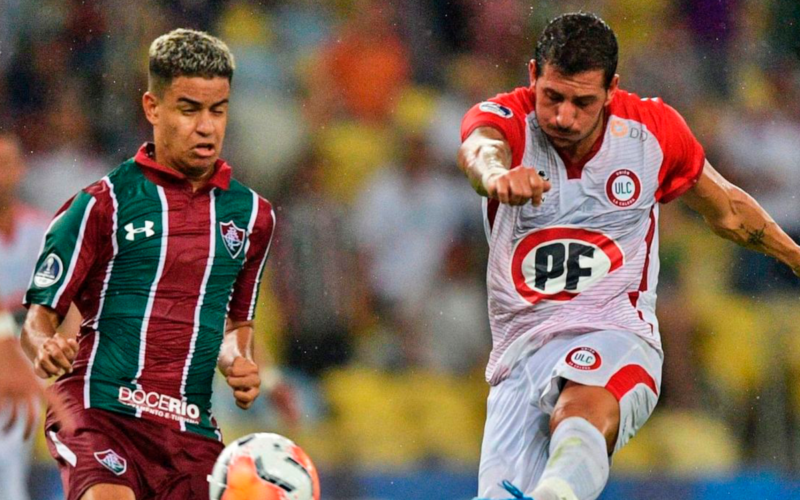 Gonzalo Castellani impactando un balón con la camiseta de Unión la Calera ante la atenta mirada de un jugador de Fluminense.