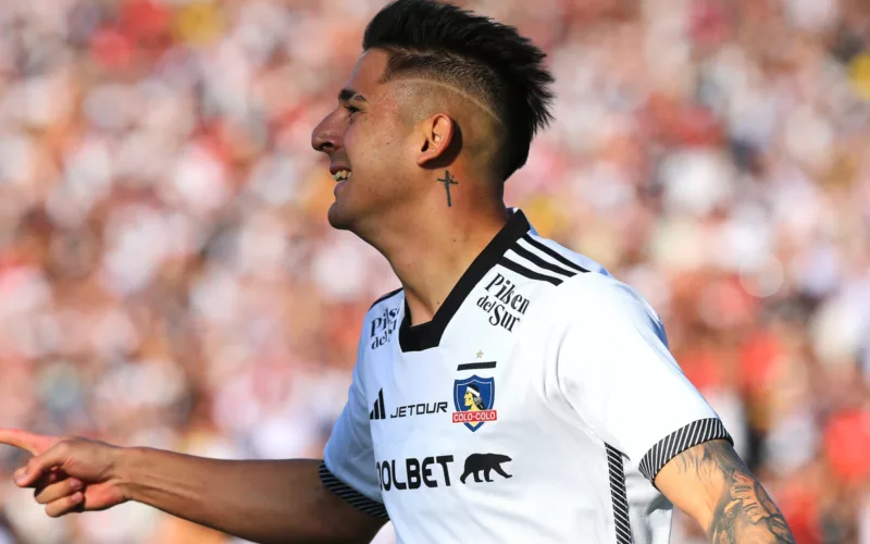 Guillermo Paiva de perfil celebra un gol con la camiseta de Colo-Colo con una notoria sonrisa en su rostro.