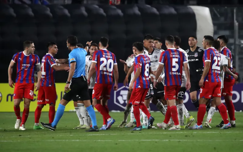 Futbolistas de Cerro Porteño rodean al árbitro Facundo Tello y reclaman un cobro, mientras que los deportistas de Colo-Colo miran atentos a la situación.