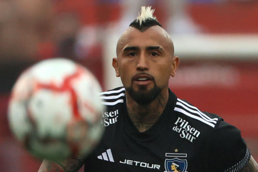 Arturo Vidal en pleno partido con la camiseta de Colo-Colo con la mirada fija puesto en un balón que va por los aires.
