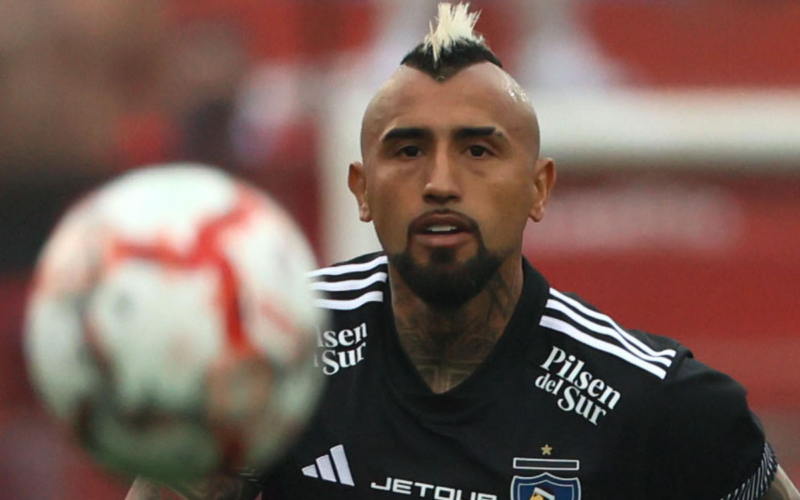 Arturo Vidal en pleno partido con la camiseta de Colo-Colo con la mirada fija puesto en un balón que va por los aires.