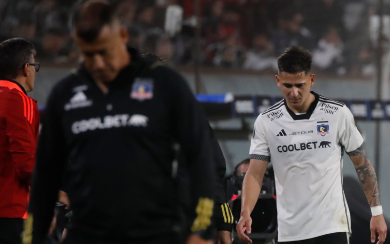 Guillermo Paiva se retira del campo de juego con claros signos de dolor, mientras que al frente suyo se encuentra Jorge Almirón, entrenador de Colo-Colo con la cabeza cabizbaja.