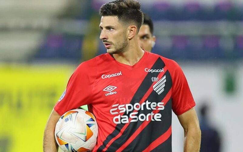 Primer plano de Lucas Di Yorio con la camiseta de Athletico Paranaense y un balón bajo su brazo.