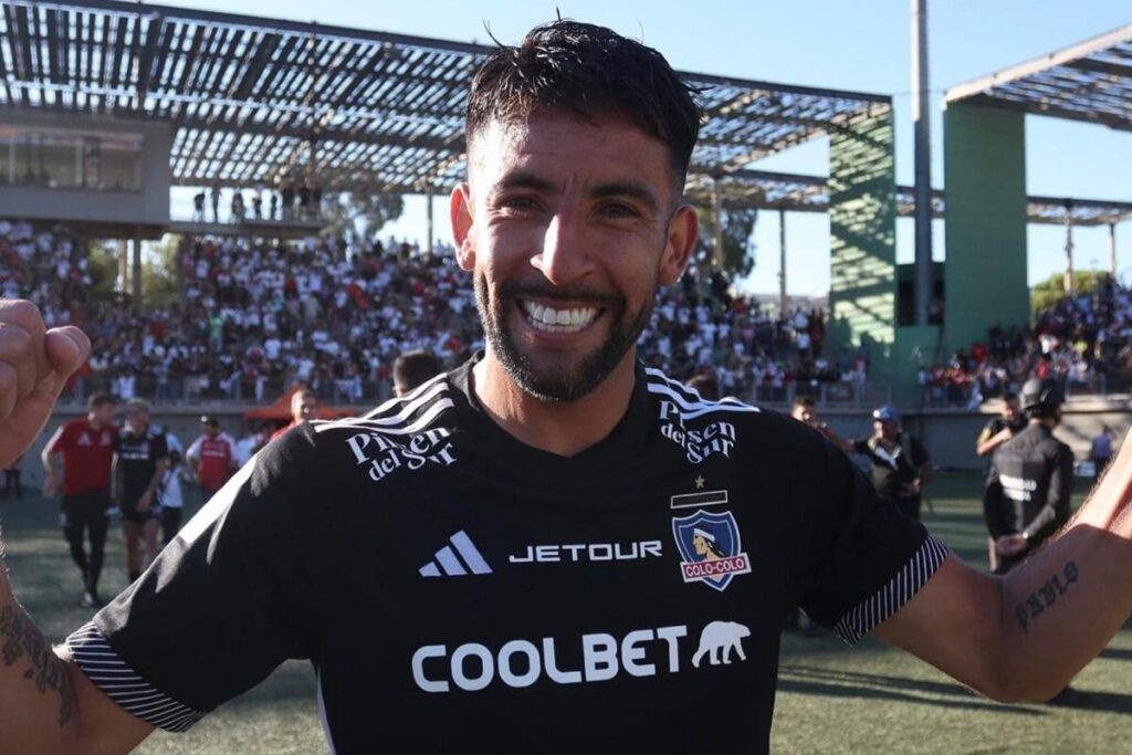 Mauricio Isla con la camiseta de Colo-Colo y los brazos en alto.