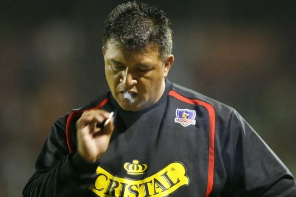 Claudio Borghi con indumentaria de Colo-Colo mientras fuma durante un partido.