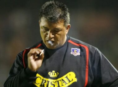Claudio Borghi con indumentaria de Colo-Colo mientras fuma durante un partido.