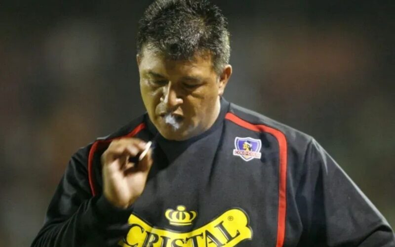 Claudio Borghi con indumentaria de Colo-Colo mientras fuma durante un partido.
