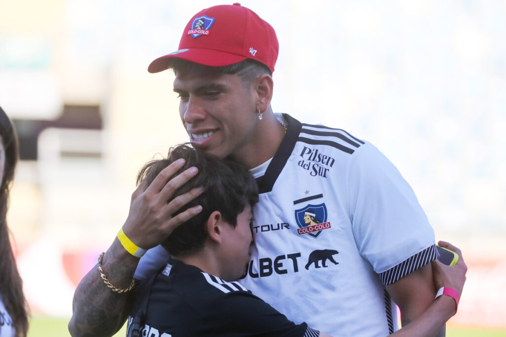 Carlos Palacios con la camiseta de Colo-Colo abrazando a un nuño.