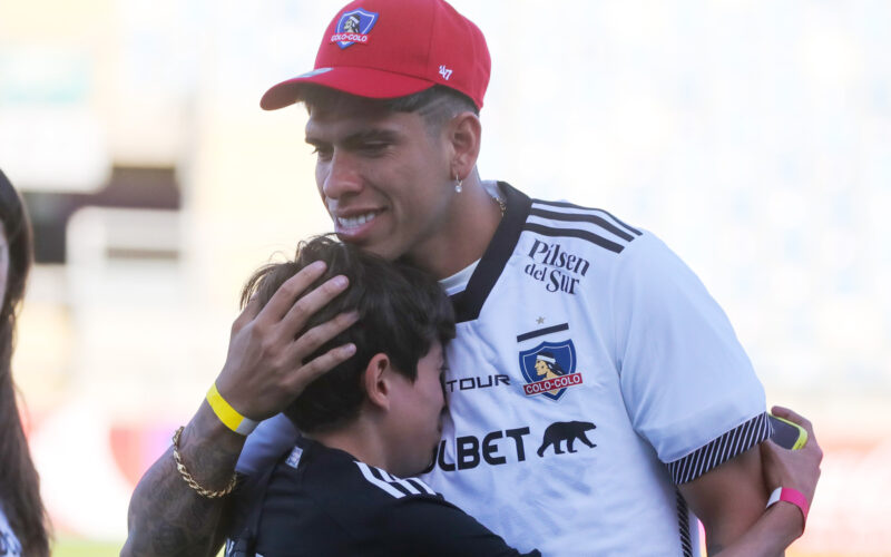 Carlos Palacios con la camiseta de Colo-Colo abrazando a un nuño.
