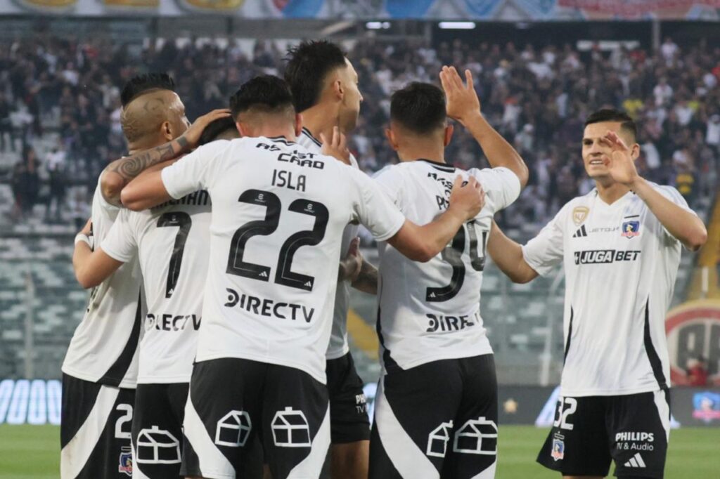 Jugadores de Colo-Colo celebrando un gol contra Unión Española con hinchas de Colo-Colo en el Estadio Monumental de fondo.