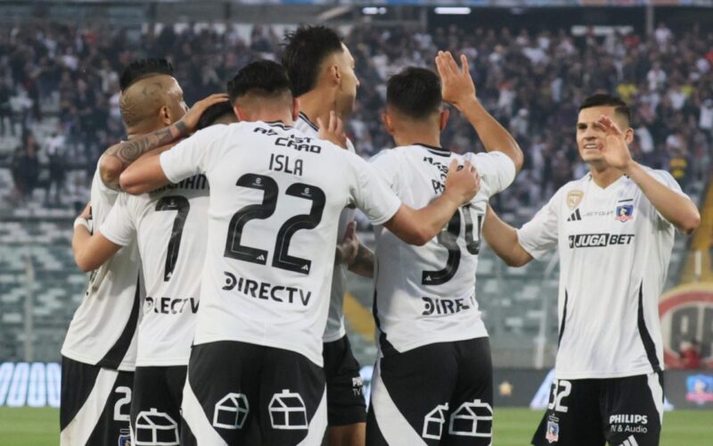 Jugadores de Colo-Colo celebrando un gol contra Unión Española con hinchas de Colo-Colo en el Estadio Monumental de fondo.