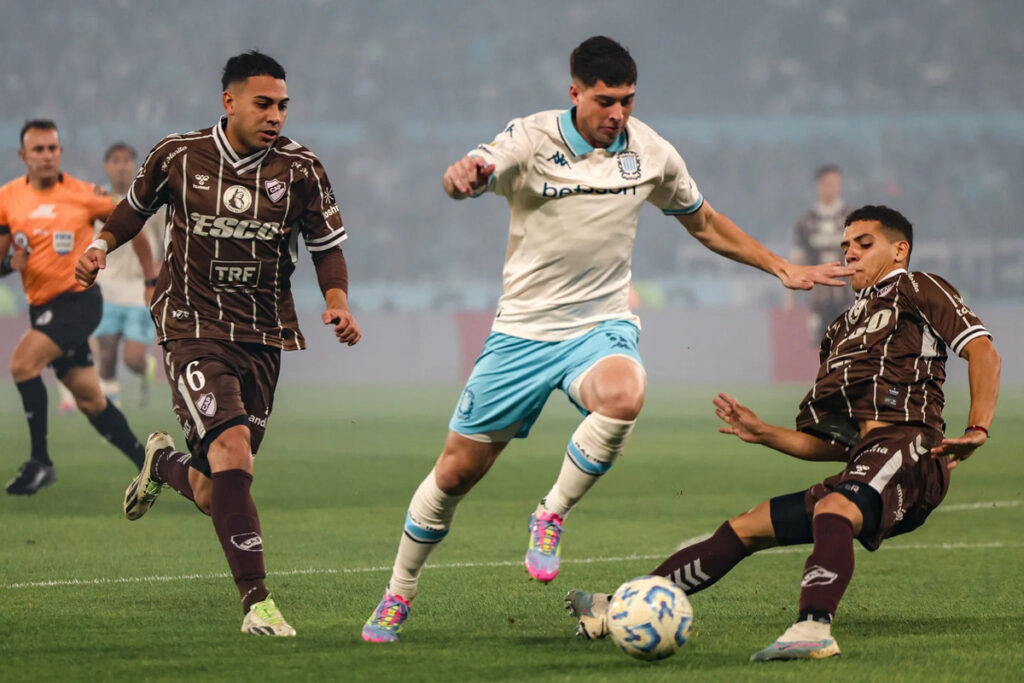 Jugador de Racing Club frente a dos futbolistas de Platense por los octavos de final del Torneo de Apertura Argentino.