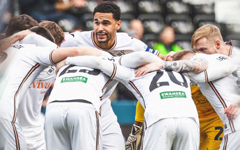 Jugadores del Swansea City reunidos con hinchas del club inglés de fondo.