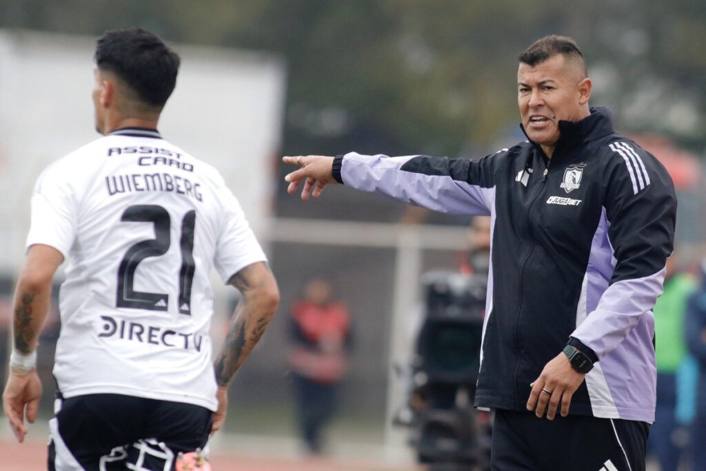Jorge Almirón dirigiendo a Colo-Colo frente a O'Higgins con Erick Wiemberg en el plano.